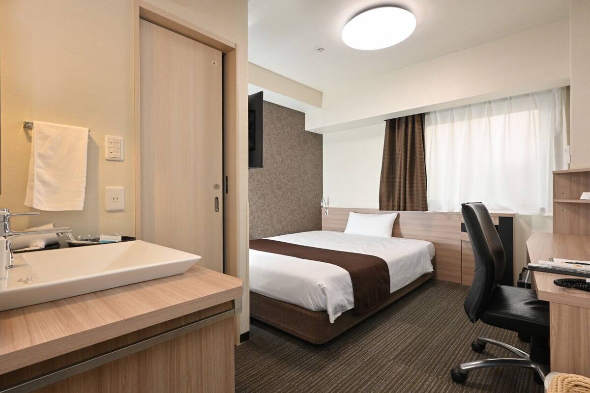 A hotel room with a bathroom, a bed, a desk, and a chair.