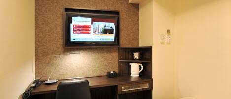 Una habitación de hotel con escritorio, televisor montado en la pared, cafetera y cama.