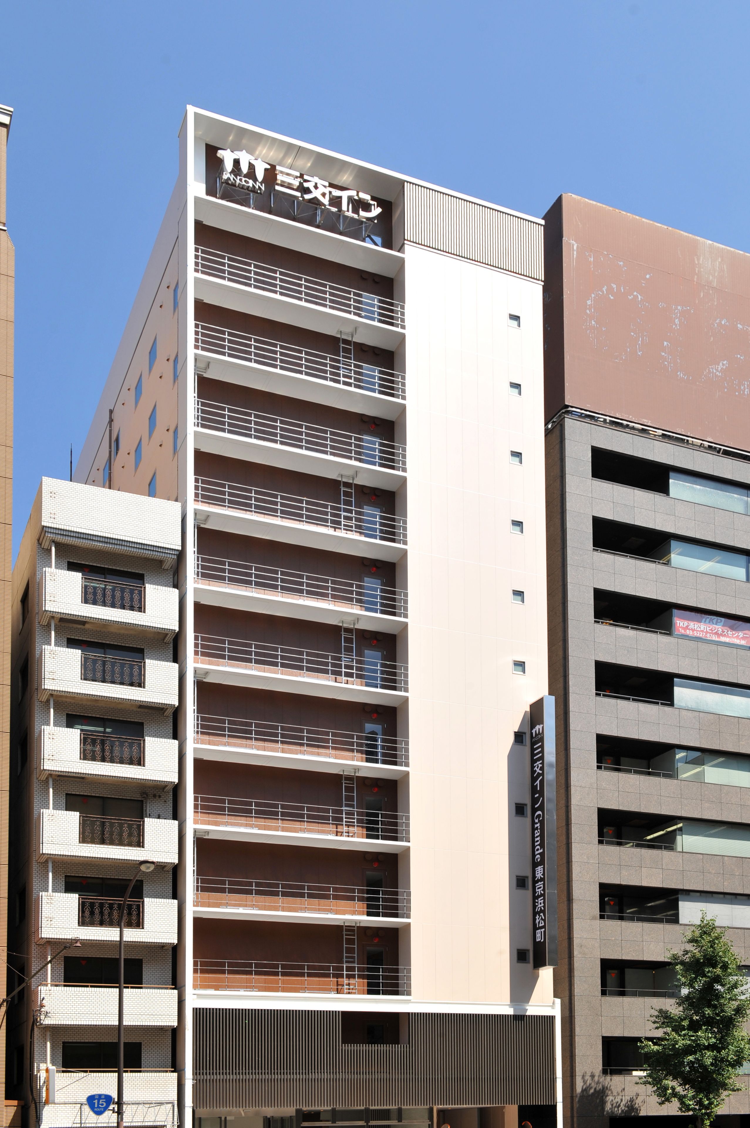 Un immeuble à plusieurs étages doté d’une architecture moderne, avec des balcons à chaque niveau et une enseigne bien visible au sommet.