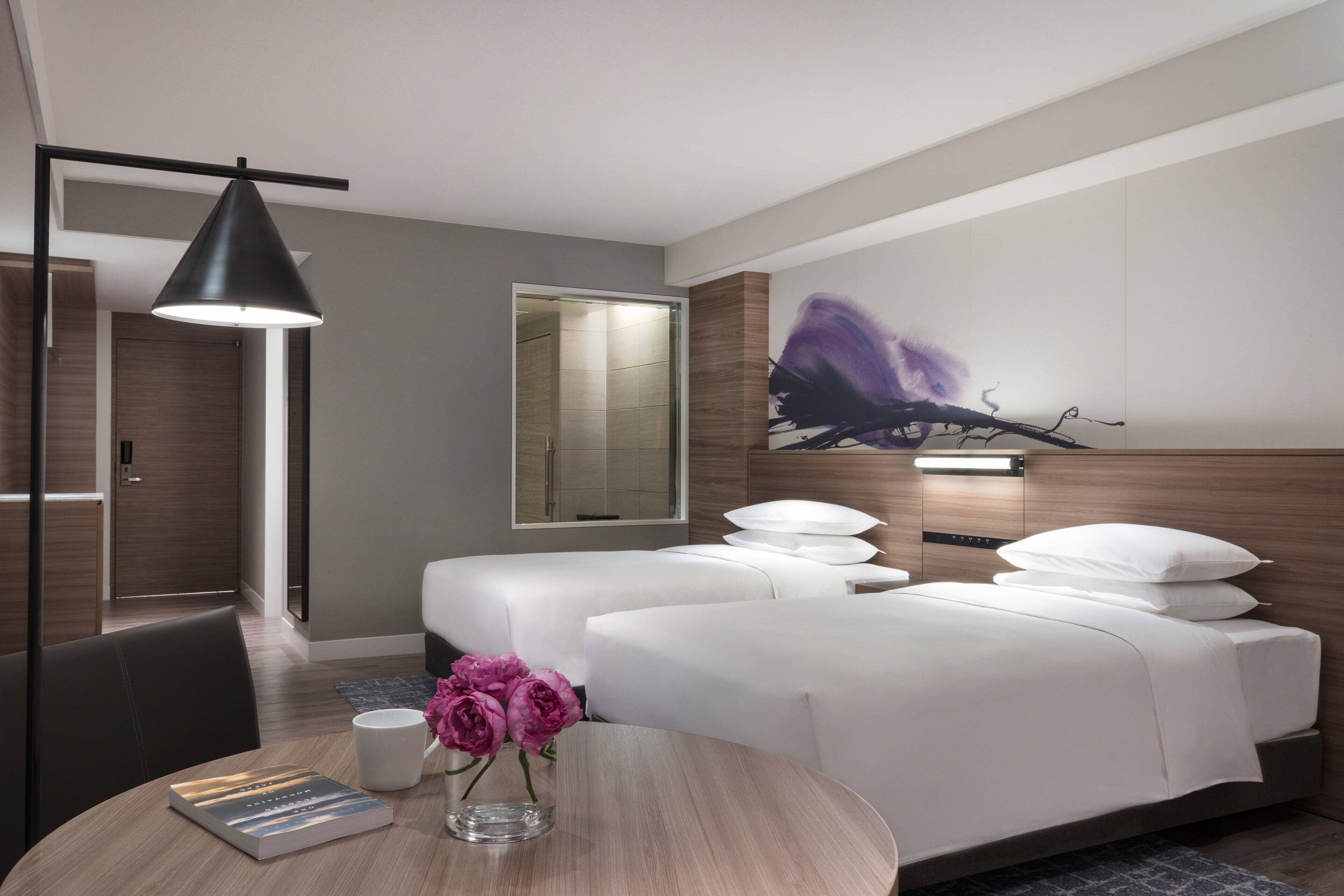 Una habitación de hotel moderna con dos camas, una mesita de noche, una lámpara, un espejo y un cuadro en la pared.