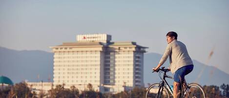 Una persona pedalea en bicicleta por un campo de césped, con un gran edificio de hotel al fondo.
