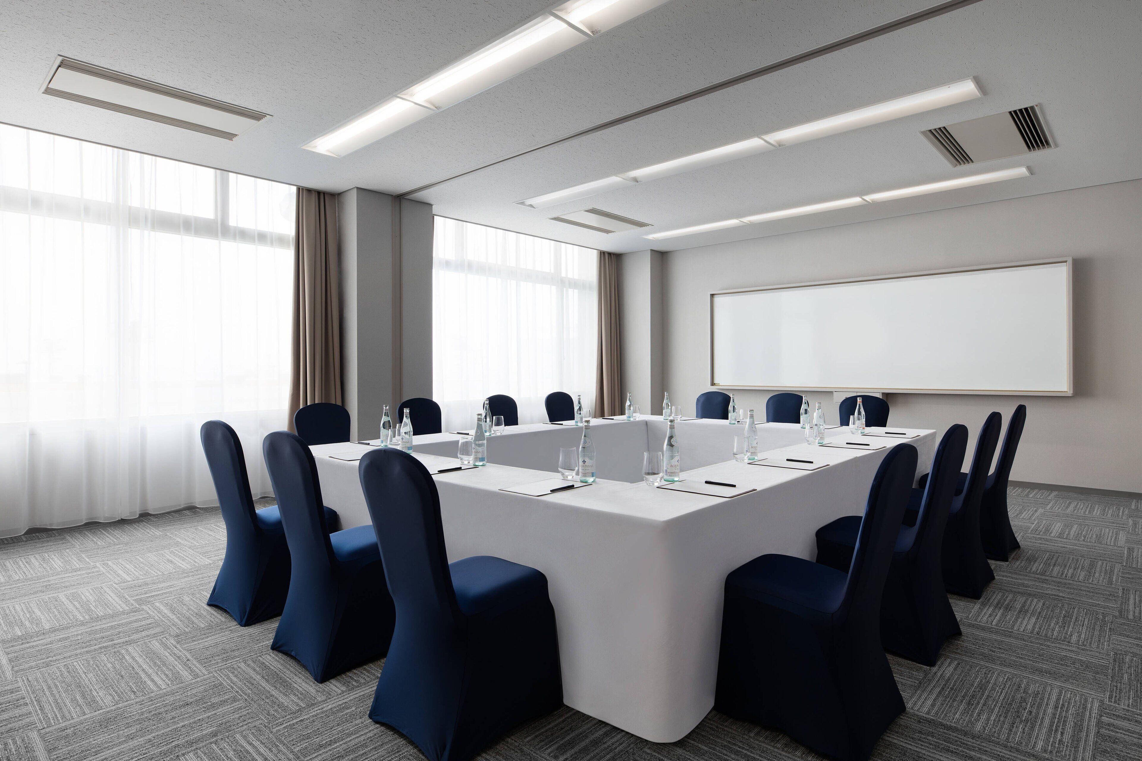 A conference room with a long table, chairs, a projector screen, and a large window.
