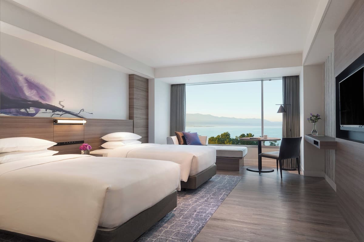 Une chambre d’hôtel moderne avec deux lits, une petite table, une chaise et un téléviseur.