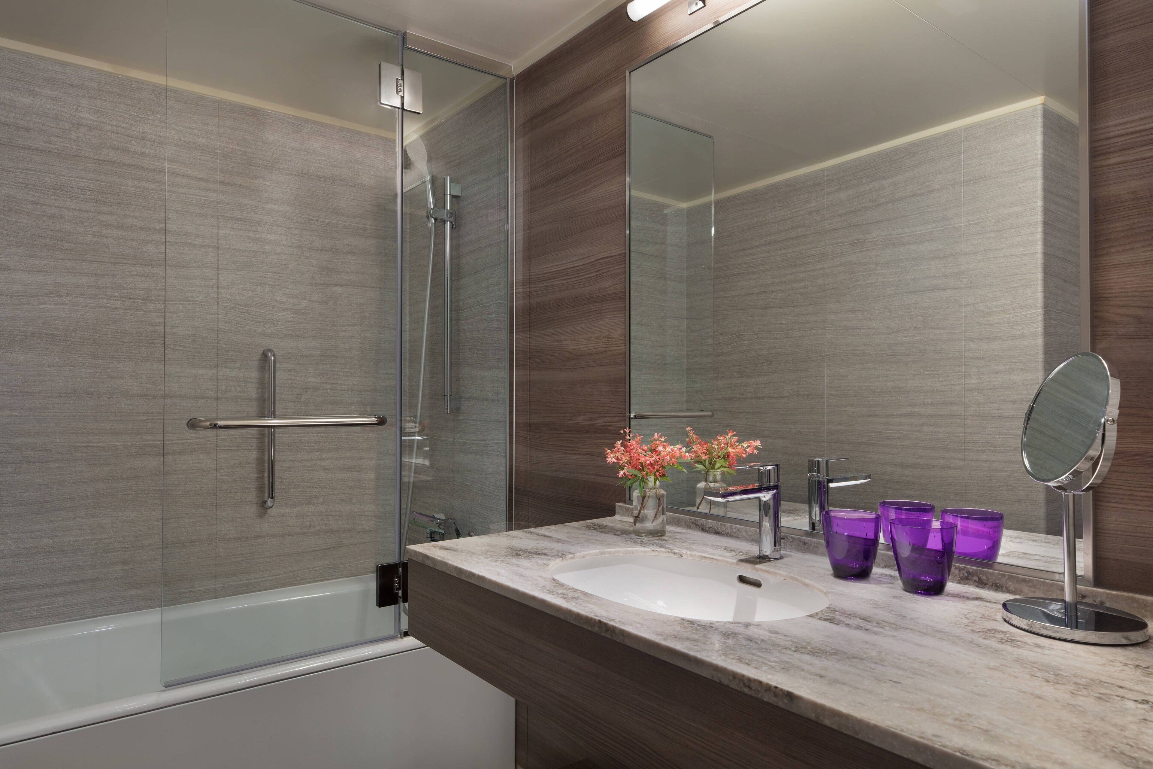 A modern bathroom with a glass shower enclosure, a marble sink, and a large mirror.