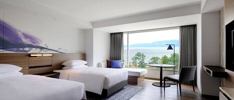 Een hotelkamer met twee bedden, een kleine tafel, een stoel en een groot raam met uitzicht op zee.