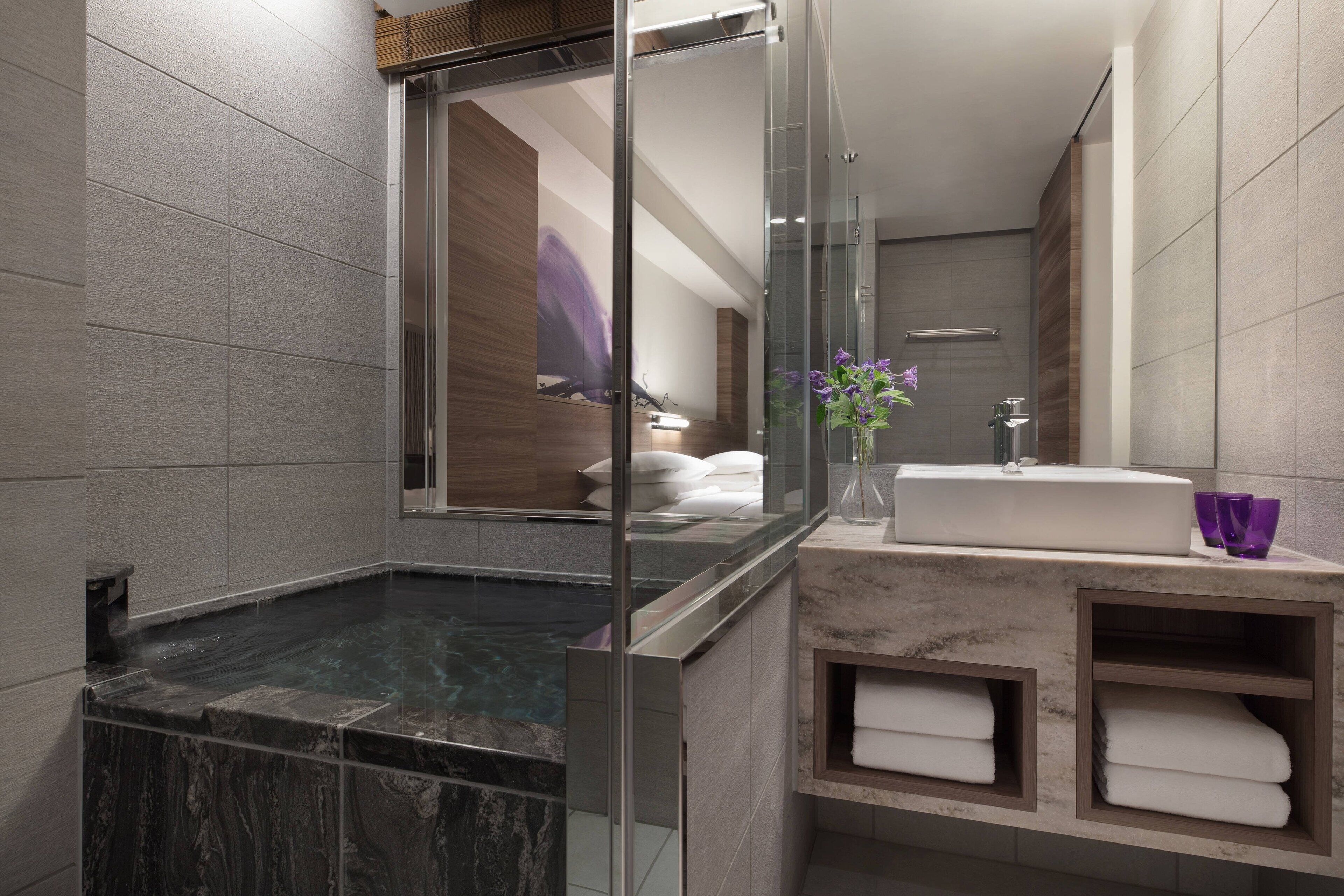 Une salle de bain moderne dotée d’une douche à parois de verre, d’une baignoire carrelée de marbre, d’un lavabo encastré et d’un meuble-vasque avec des étagères pour les serviettes.