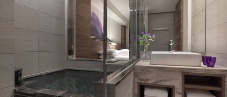Une salle de bain moderne dotée d’une douche à parois de verre, d’une baignoire carrelée de marbre, d’un lavabo encastré et d’un meuble-vasque avec des étagères pour les serviettes.