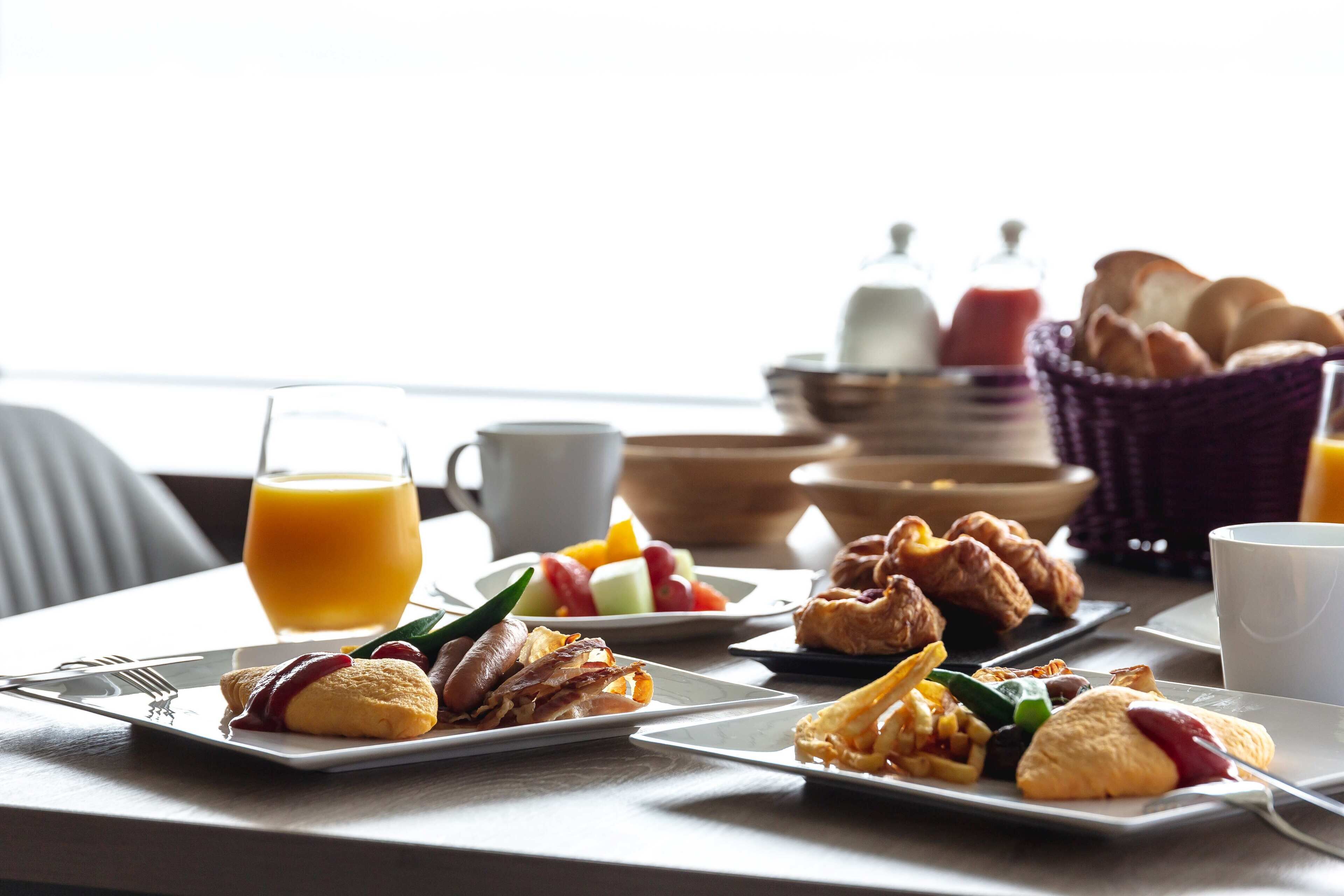 Une table de petit-déjeuner avec des assiettes remplies de nourriture, un verre de jus d’orange et un panier de pain.