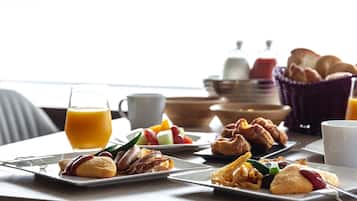 A breakfast table with plates of food, a glass of orange juice, and a basket of bread.