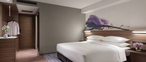 Una habitación de hotel moderna con una cama grande, un armario de madera, un escritorio con una silla y una obra de arte en la pared.