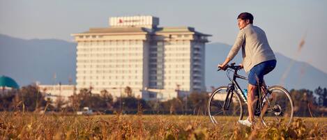 Una persona pedaleando en un campo con un edificio grande al fondo.