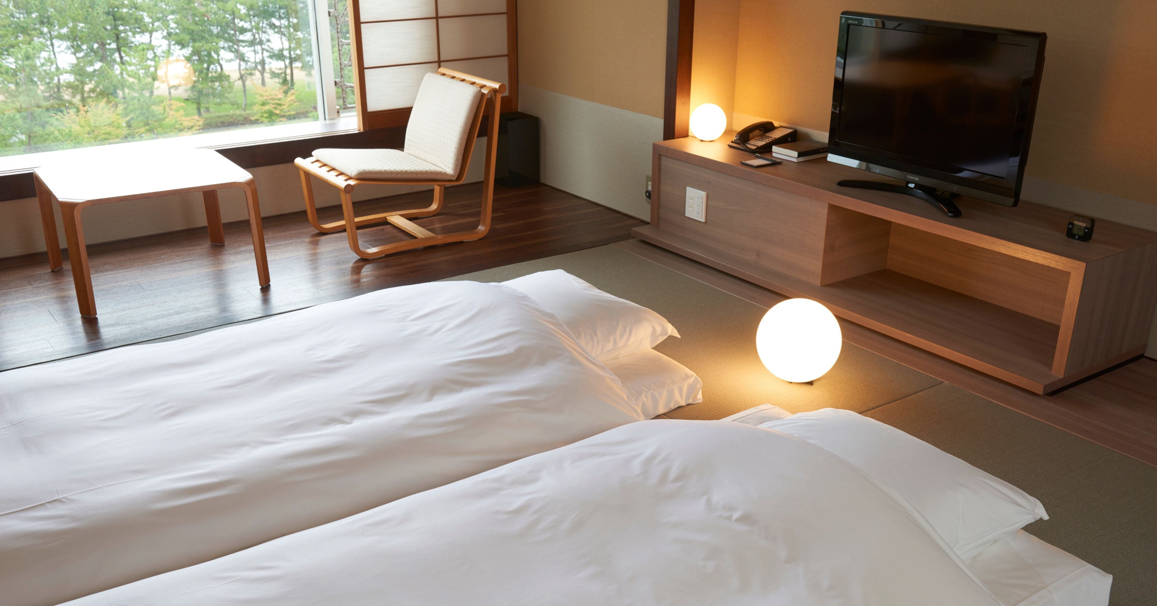 Habitación de hotel con dos camas, un escritorio, una silla, un televisor y una lámpara de noche.