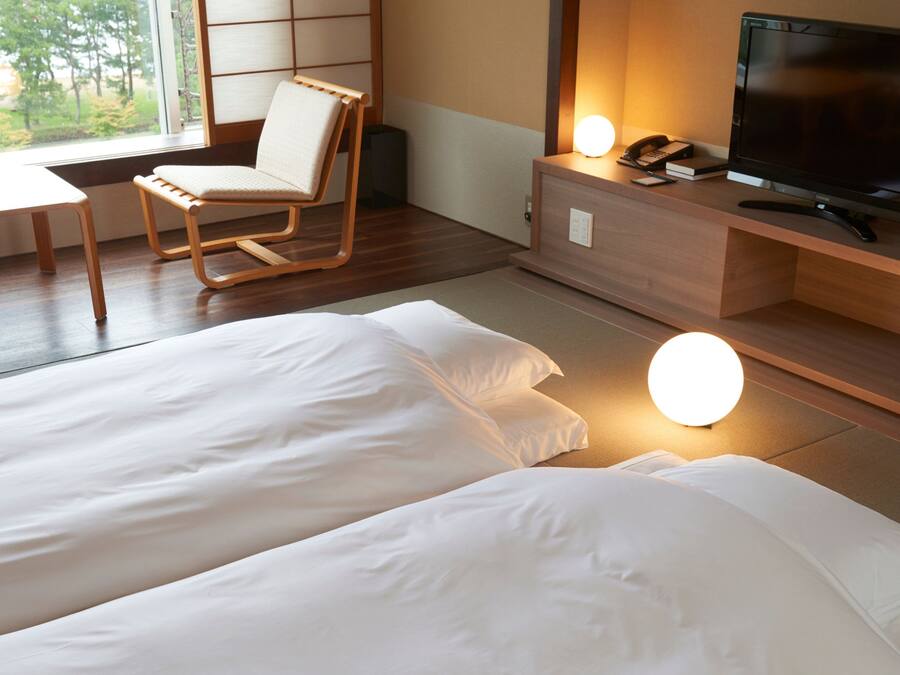 Habitación de hotel con dos camas, un escritorio, una silla, un televisor y una lámpara de noche.