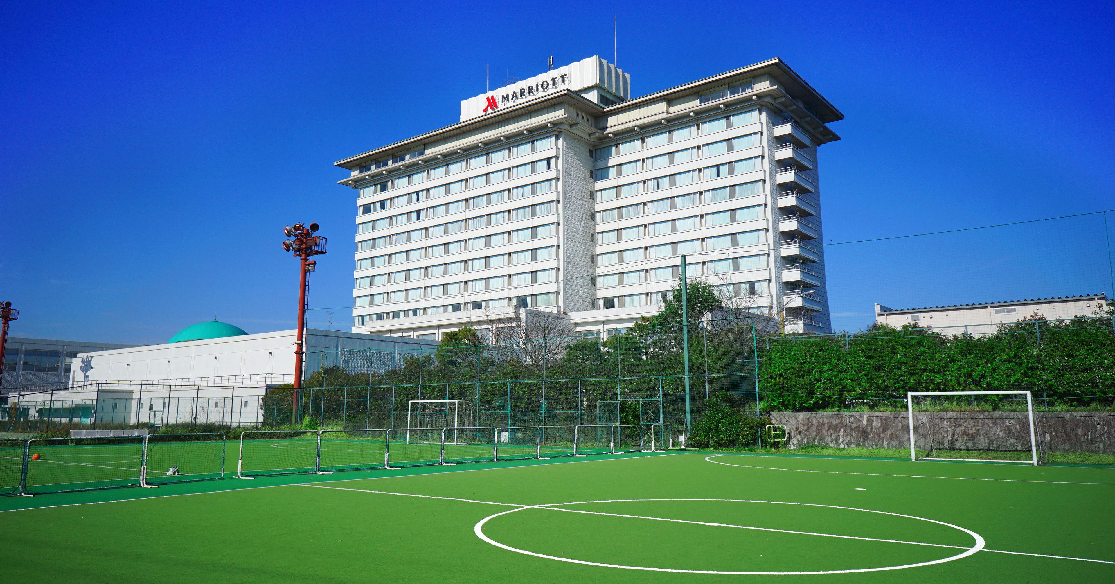 A multi-story hotel with a Marriott sign, surrounded by a fenced sports field with a goalpost.