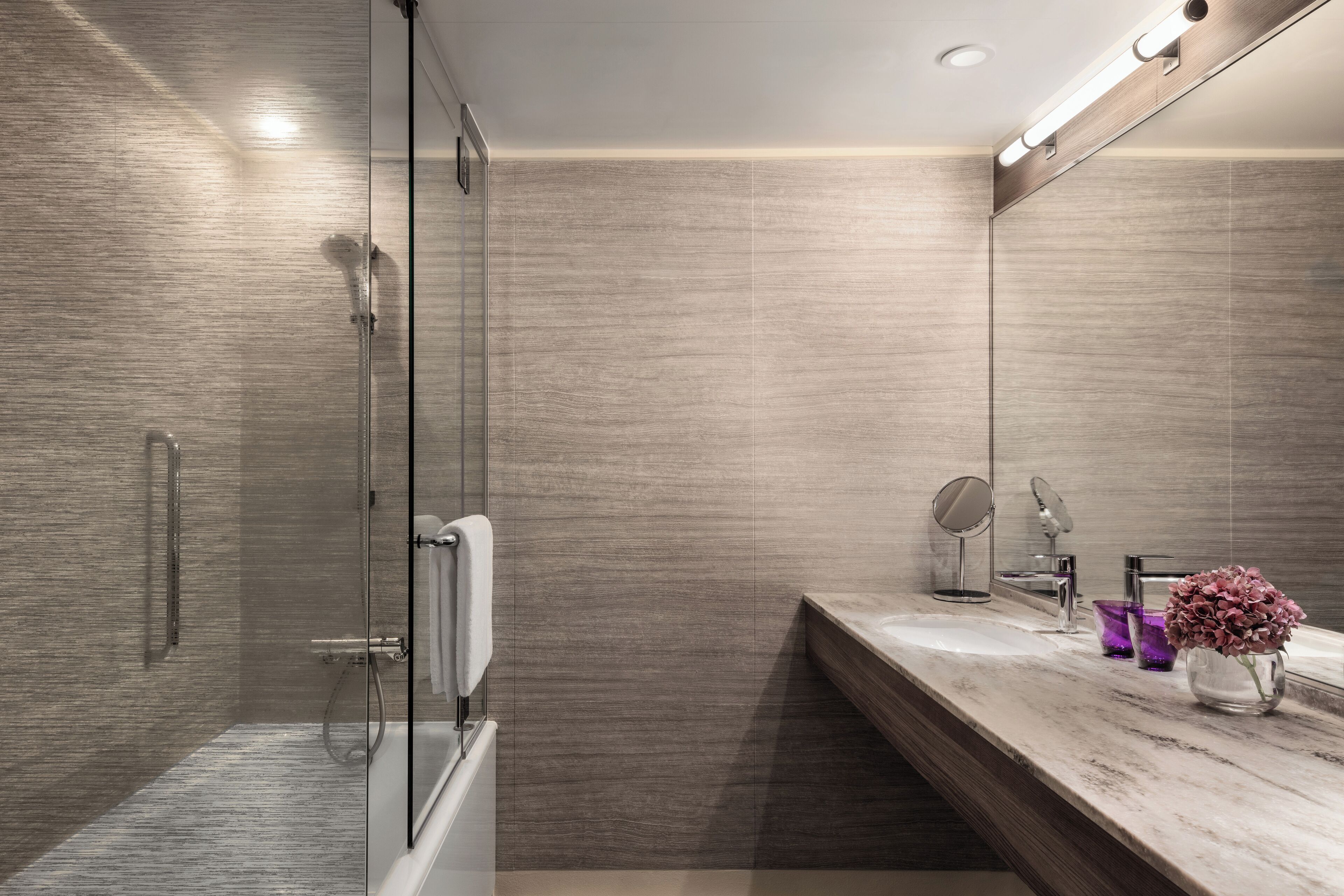 A modern bathroom with a glass shower enclosure, a marble countertop, and a mirror.