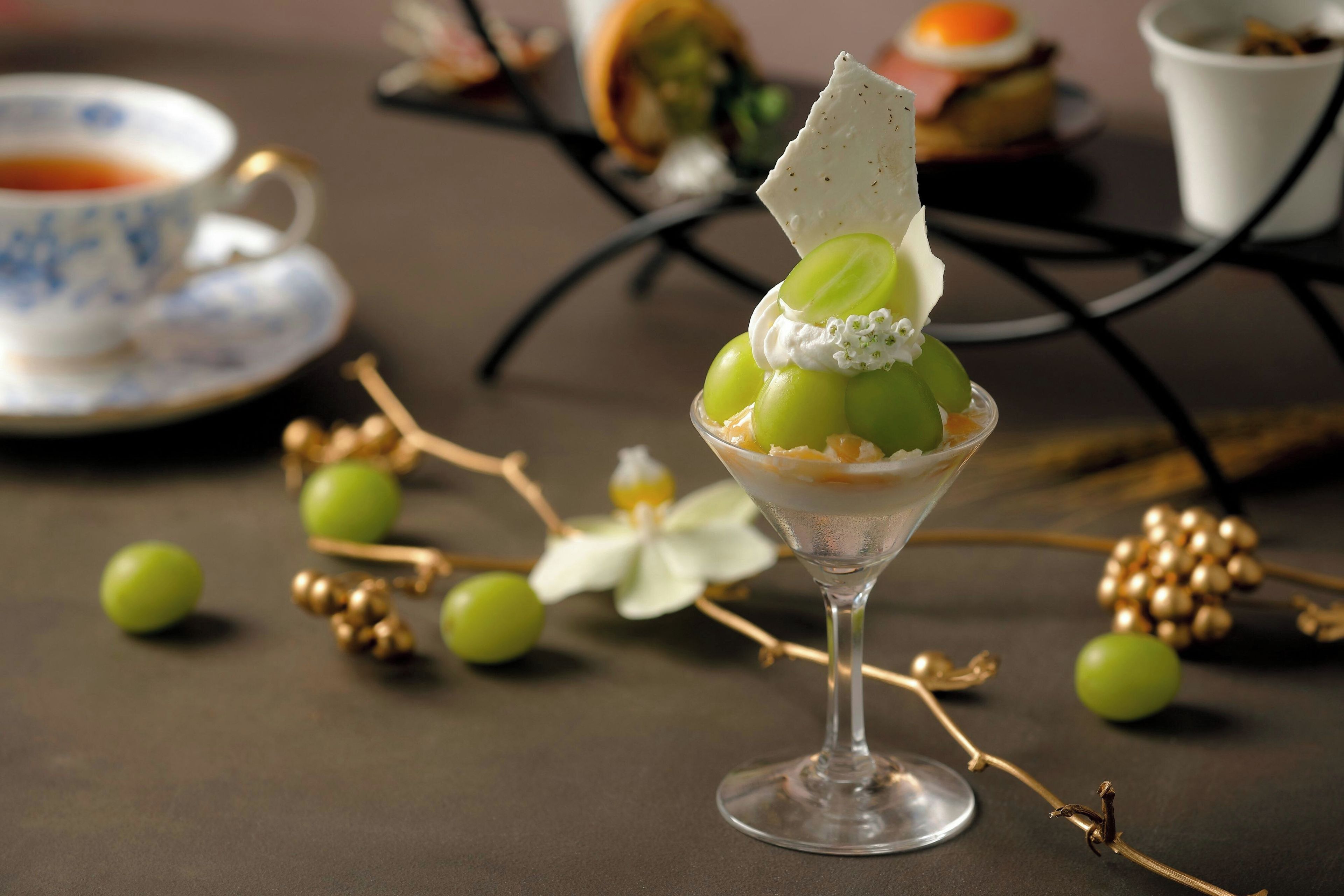 A dessert in a glass on a table with a cup and saucer in the background.