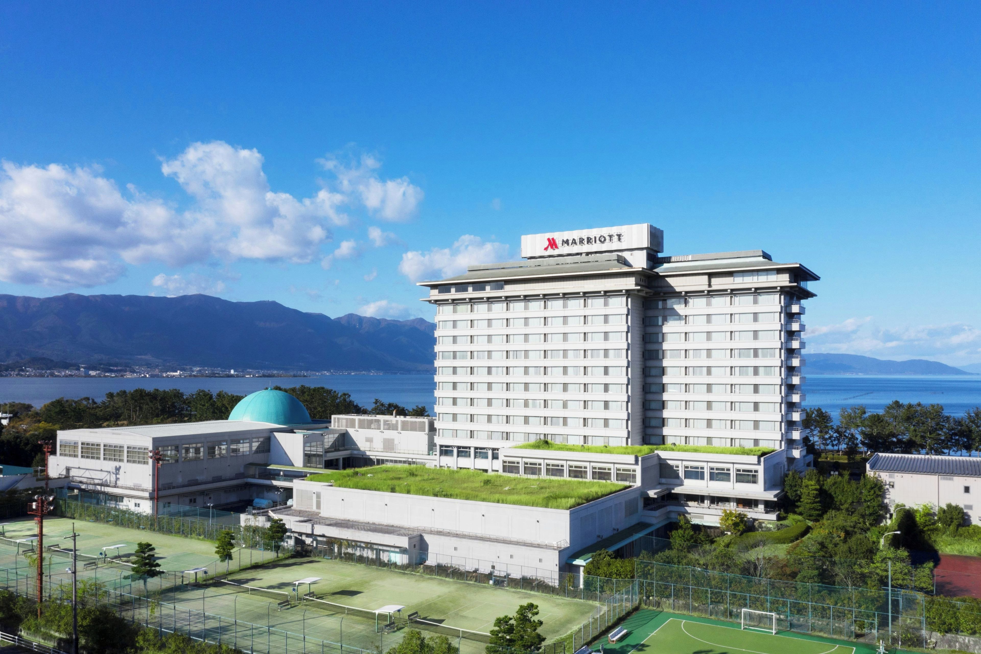 A multi-story hotel with a rooftop garden and a view of the sea.