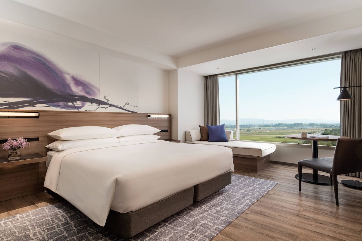 Une chambre d’hôtel moderne avec un grand lit, un coin salon offrant une belle vue et une grande fenêtre.