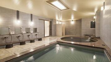 A modern indoor pool area with a rectangular pool, multiple shower stations, and a large hot tub.