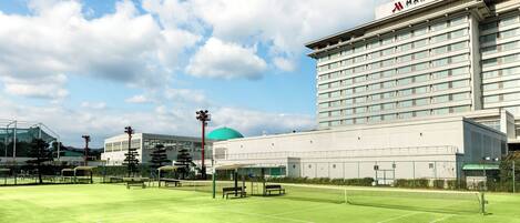 Una cancha de tenis con red, bancos y un hotel Marriott al fondo.