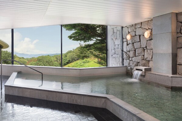 A hot tub with a waterfall feature, large windows offering a view of a mountainous landscape, and stone wall accents.