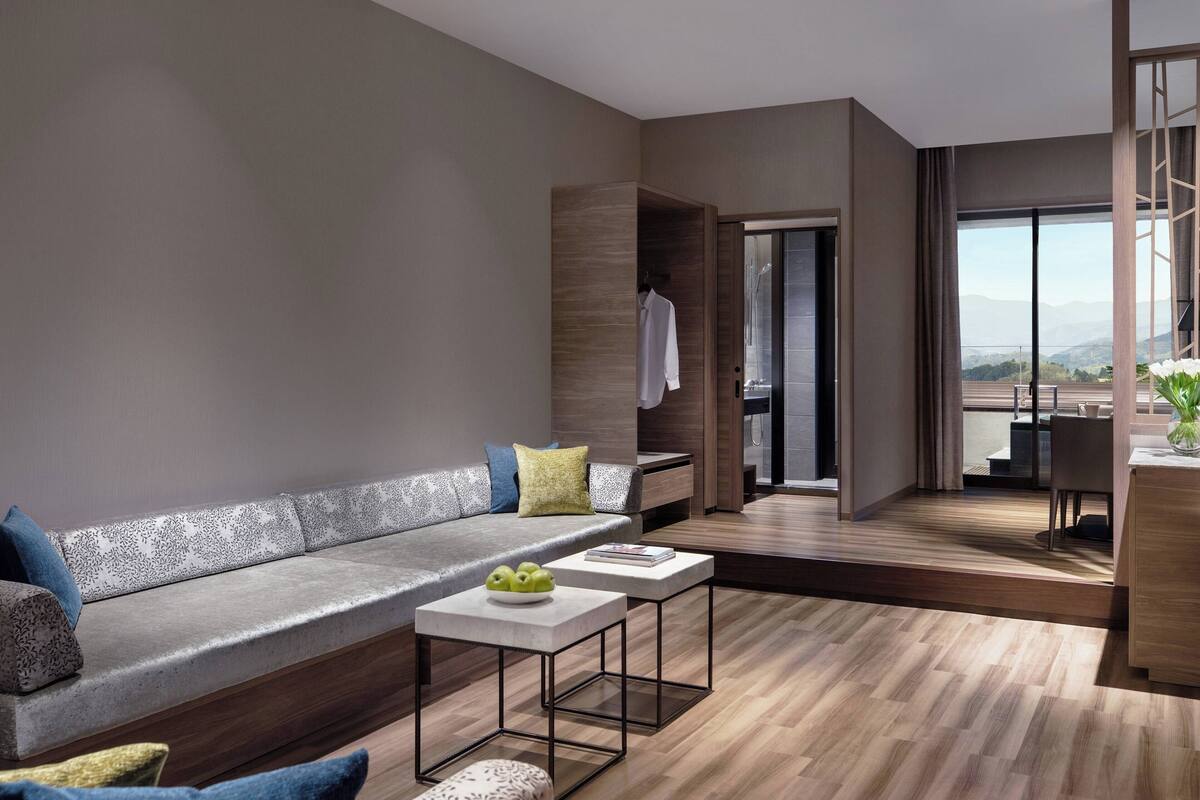 A modern living room with a sofa, a coffee table, and a view of a balcony with a table and chairs.