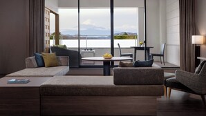 Een moderne woonkamer met een groot raam, een bank, een ronde tafel met een fruitschaal en een stoel.