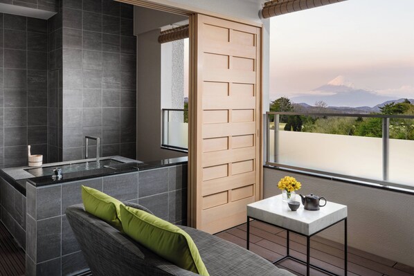 A modern bathroom with a bathtub, a toilet, and a shower area. There is a balcony with a view of a mountain. - Izu Marriott Hotel Shuzenji (Izu)
