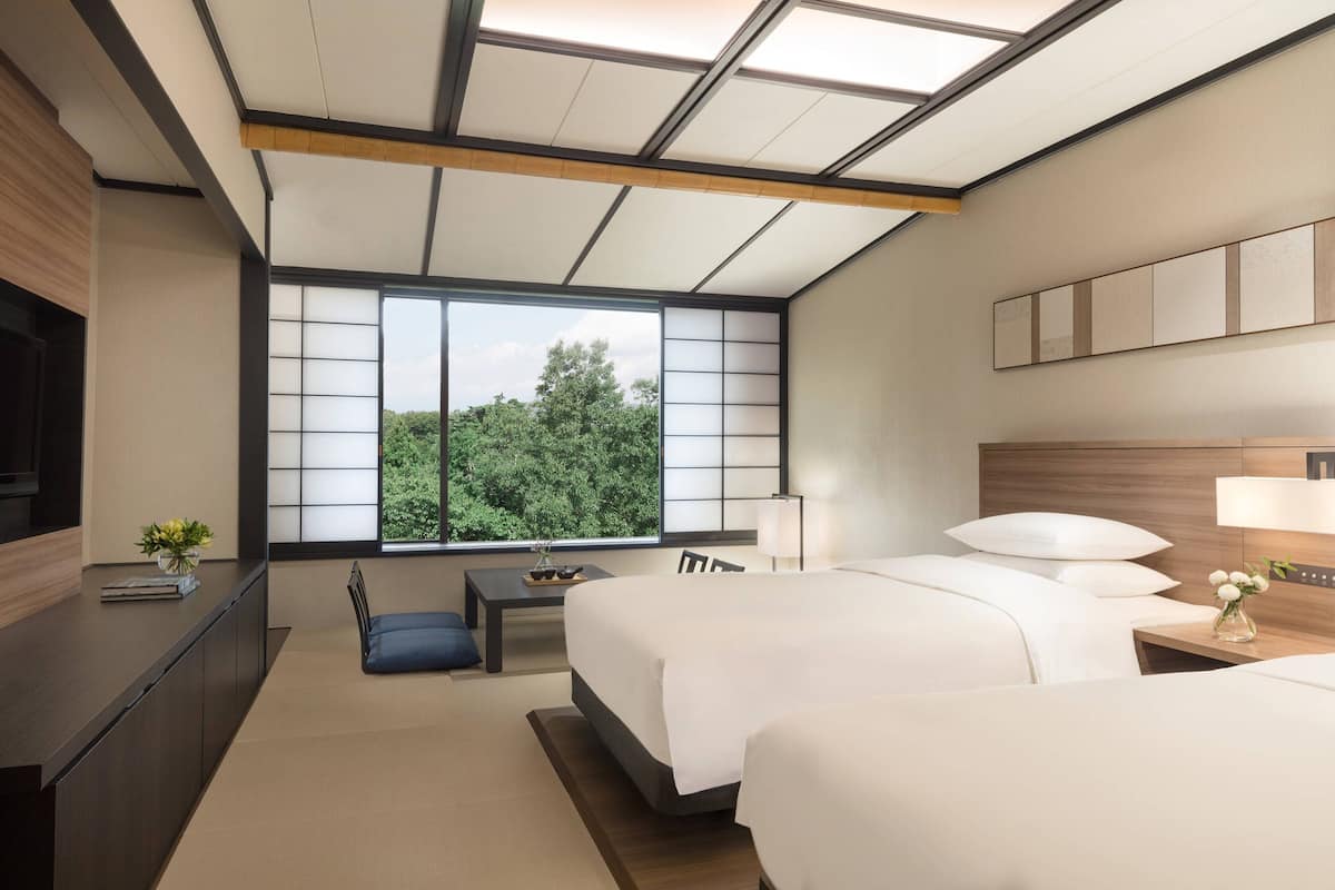 A modern hotel room with a large window, a bed, a desk, and a TV.