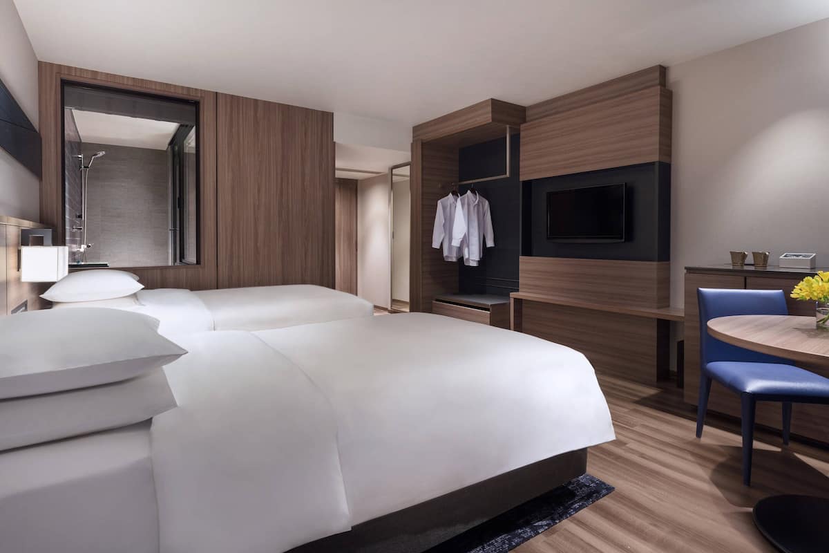 A modern hotel room with a large bed, a desk with a chair, a TV, and a mirror.