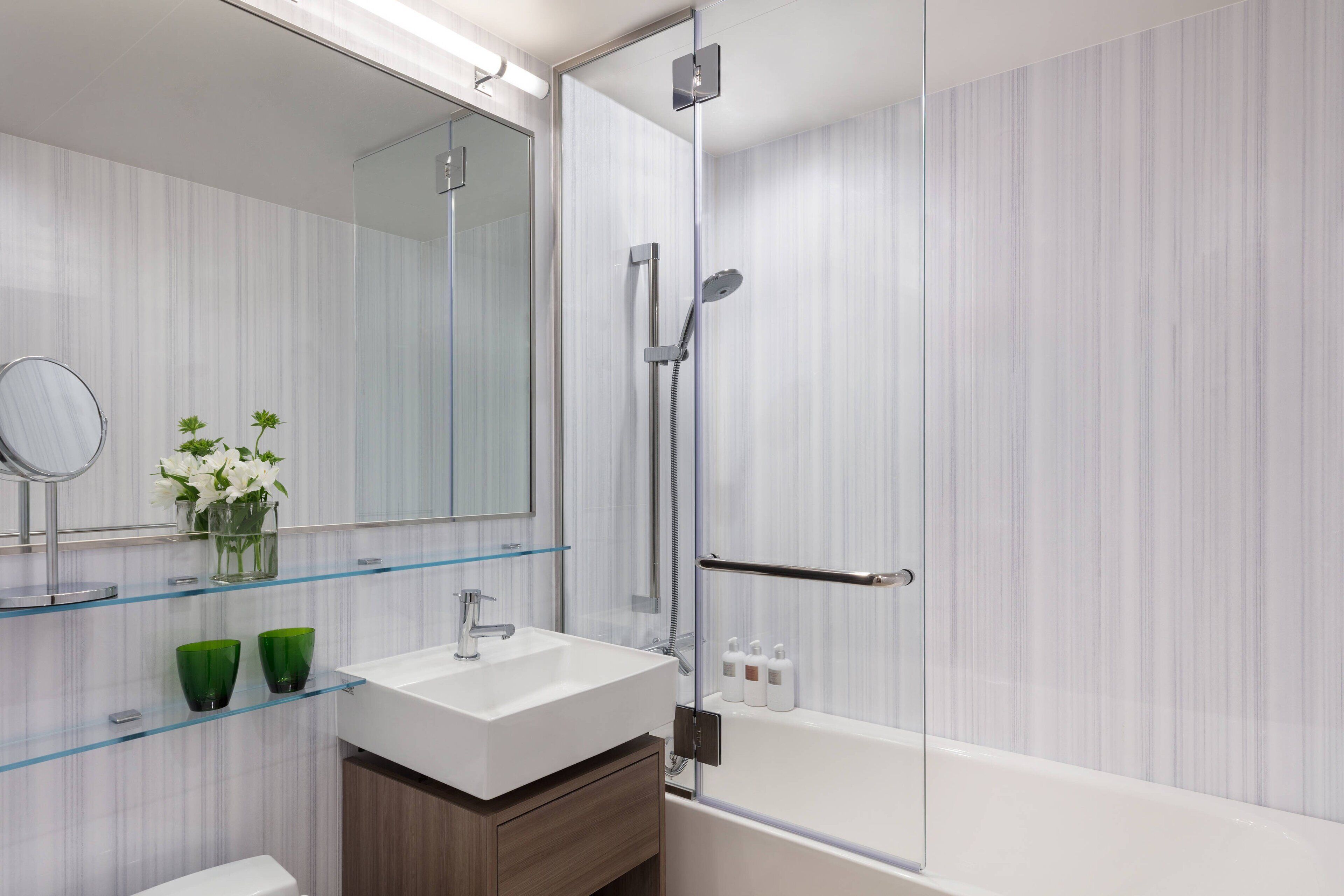 A modern bathroom with a glass shower enclosure, a white sink, and a mirror.
