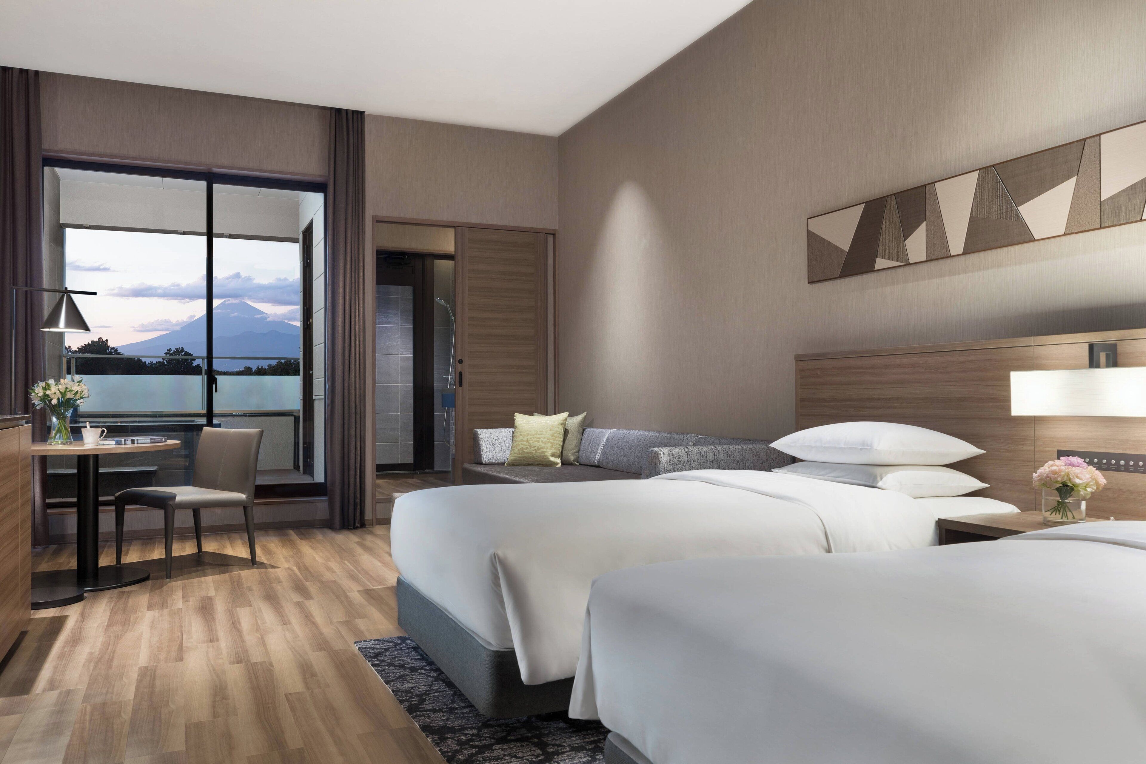 Habitación de hotel con dos camas, un escritorio con silla, un ventanal con vistas a la montaña y un diseño moderno.