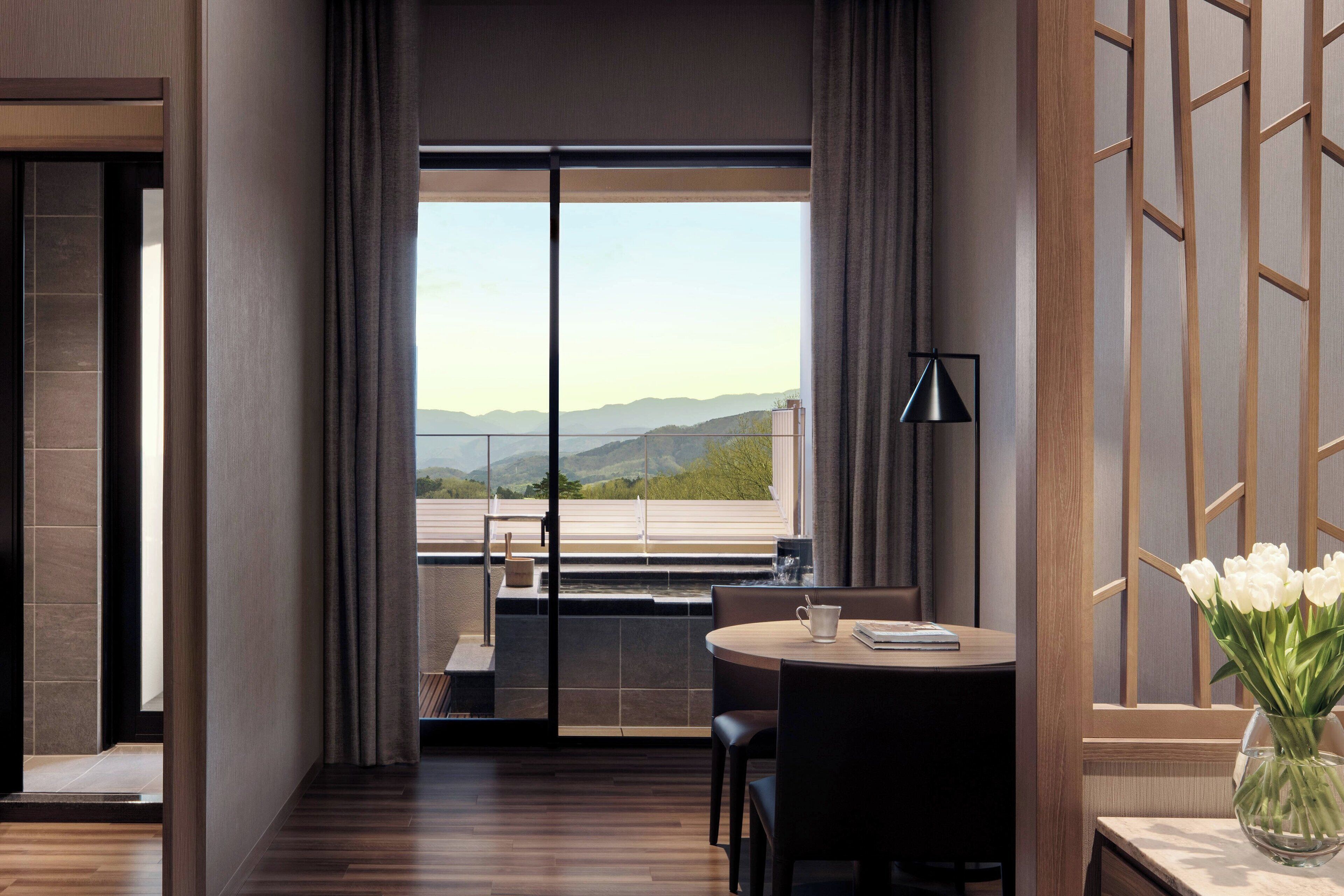 A modern hotel room with a large window, a round table, and a vase of flowers.