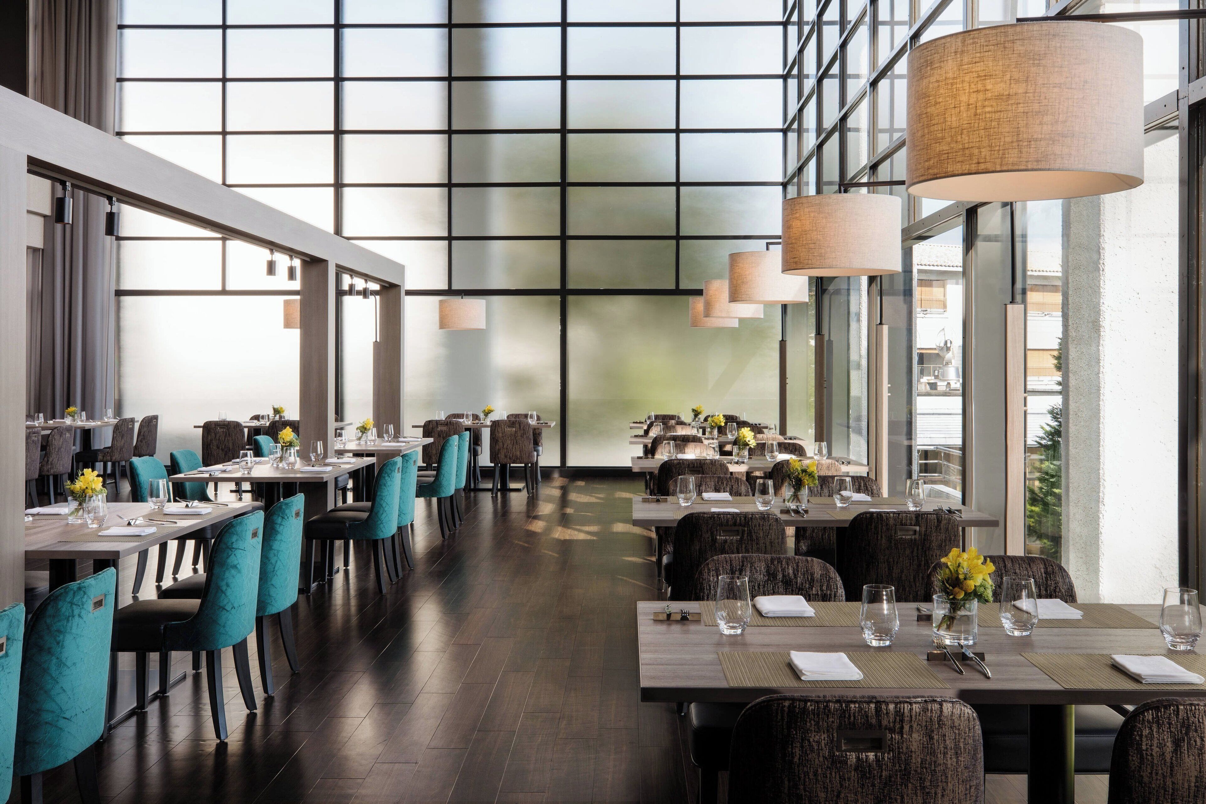 A modern dining area with long tables, chairs, and hanging lamps.