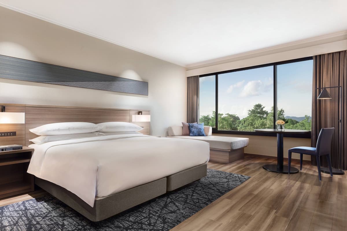 A modern hotel room with a large bed, a desk, and a view of the outdoors.