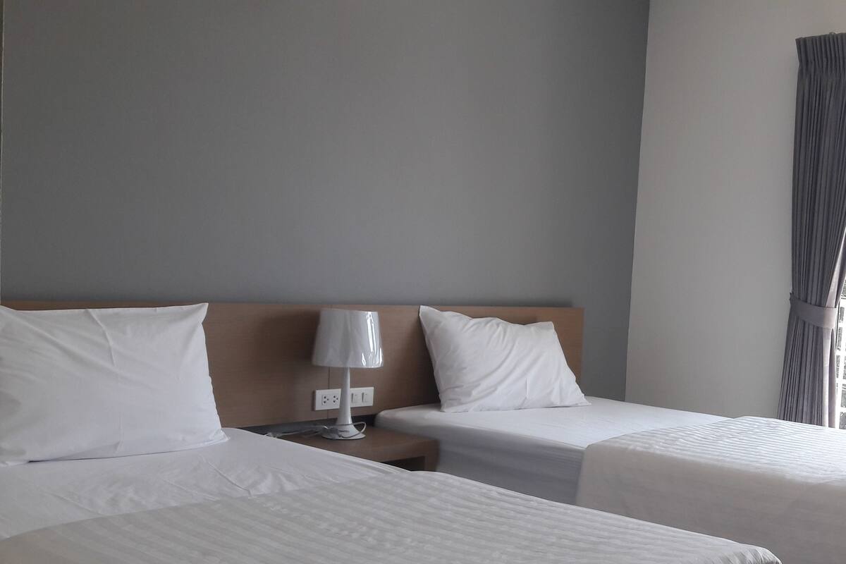 A hotel room with two beds, a nightstand with a lamp, and a window with curtains.