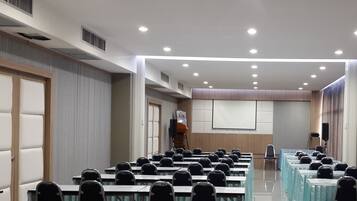 A conference room with rows of tables and chairs, a projector screen, and a podium.
