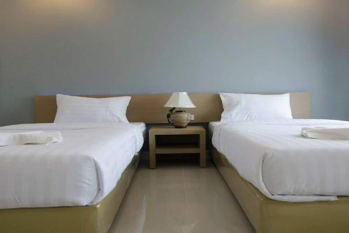 A hotel room with two single beds, a nightstand with a lamp, and a plain wall.