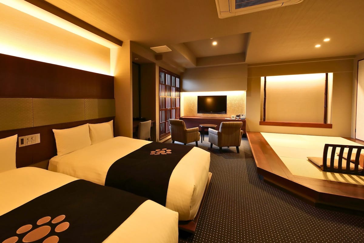 A hotel room with two beds, a desk, a TV, and a seating area.