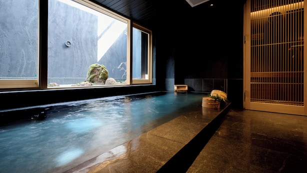 A serene indoor pool area with a wooden floor, a stone wall, and a large window.