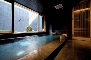 A serene indoor pool area with a wooden floor, a stone wall, and a large window. - Ryotei Matsuya Honkan Suizenji (Kumamoto)