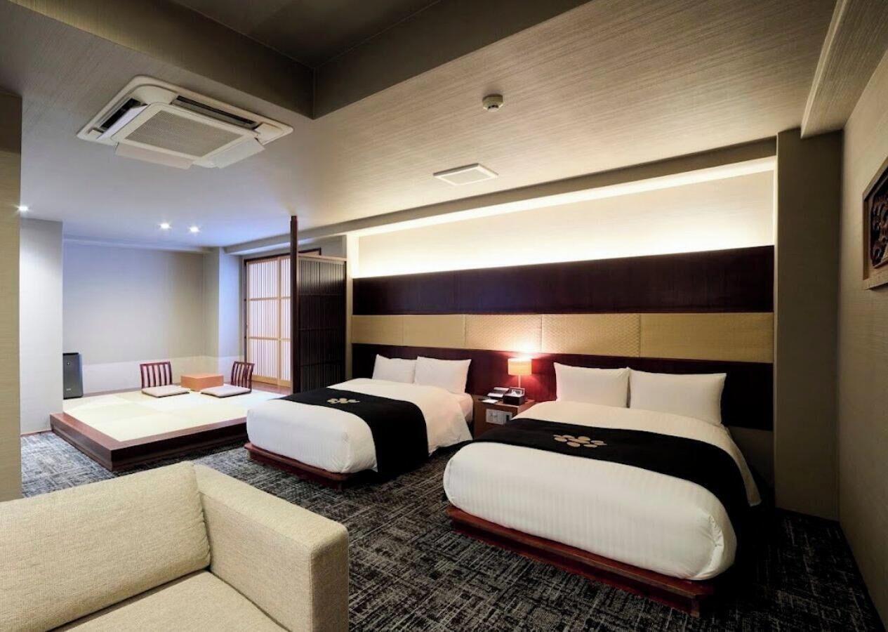 Habitación de hotel con dos camas, un sofá, una mesita de noche y un aire acondicionado.