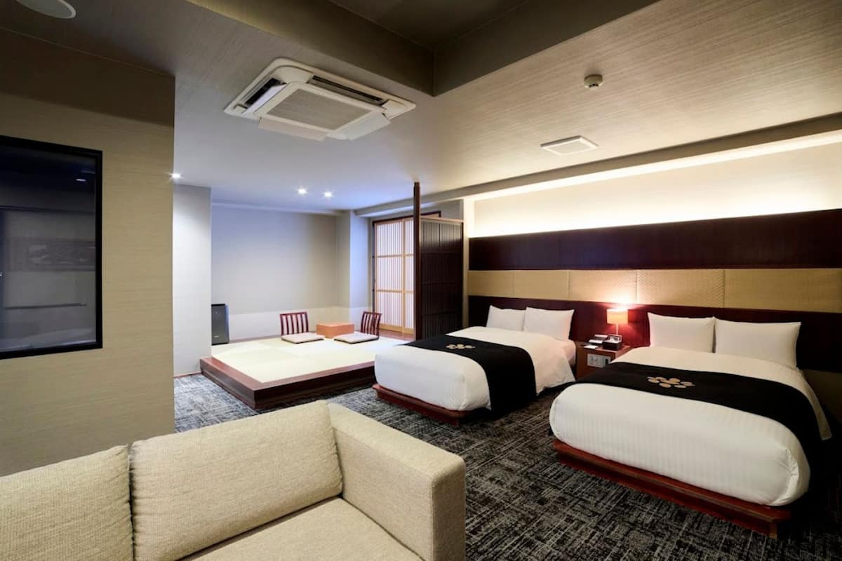 Une chambre d’hôtel avec deux lits, un canapé, un bureau et une grande fenêtre.