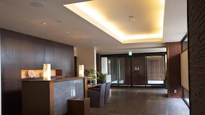 A modern reception area with a wooden reception desk, seating, and a large window with blinds.