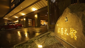 A building entrance with a stone wall, a red car parked outside, and illuminated interior lights.