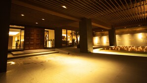 An indoor area with a tiled floor, wooden ceiling panels, and a wall with recessed lighting.