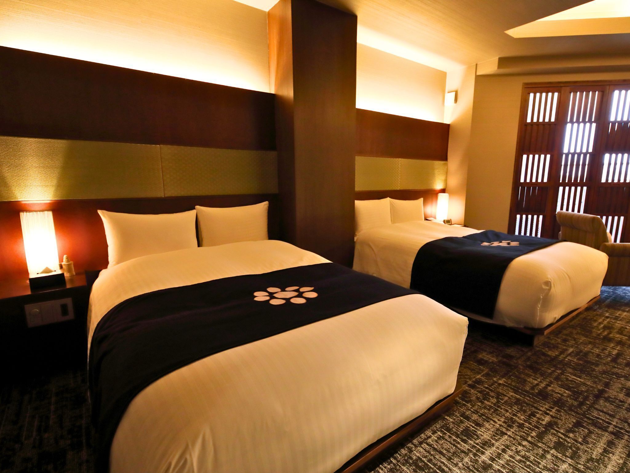 Habitación de hotel con dos camas, cada una con cabecera, mesita de noche y lámpara.