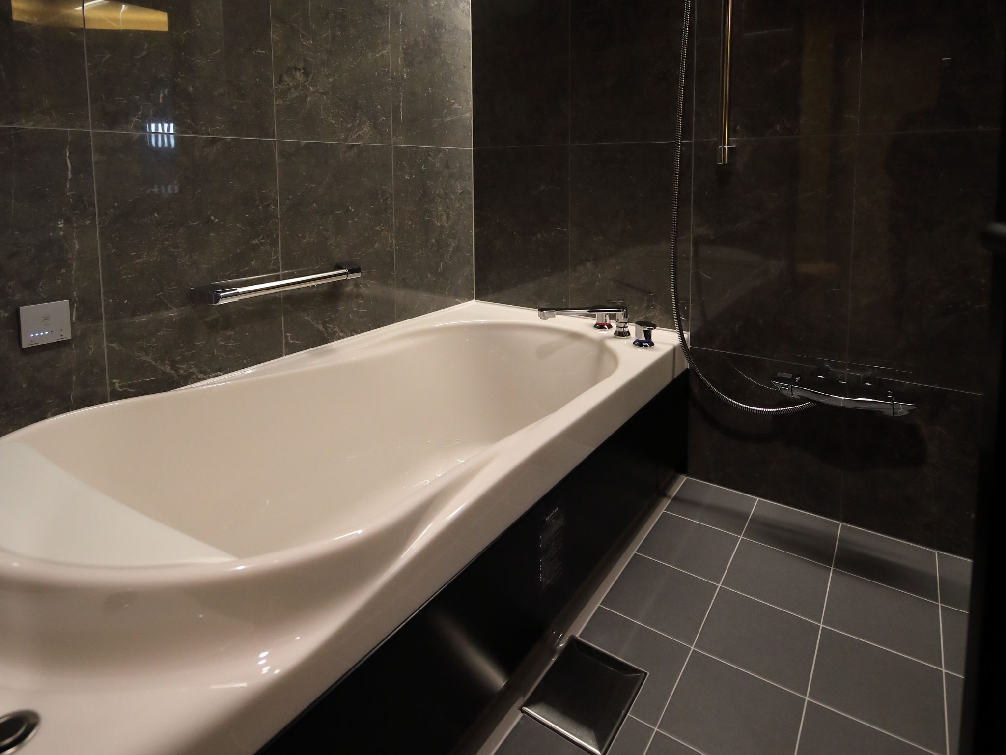 A modern bathroom with a freestanding bathtub, a handheld showerhead, and a control panel on the wall.