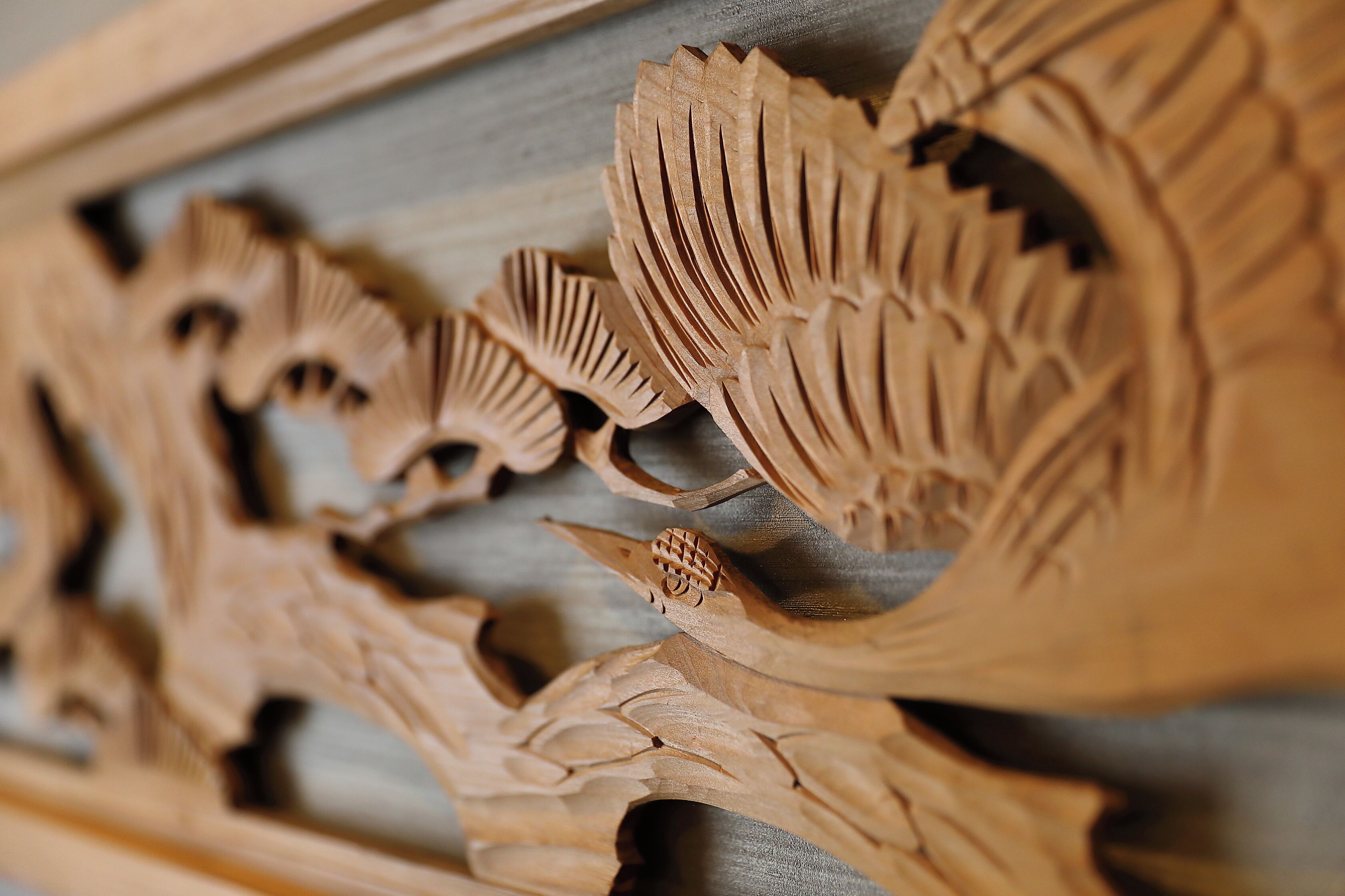 Close-up de uma escultura em madeira com desenhos detalhados de folhas e penas.