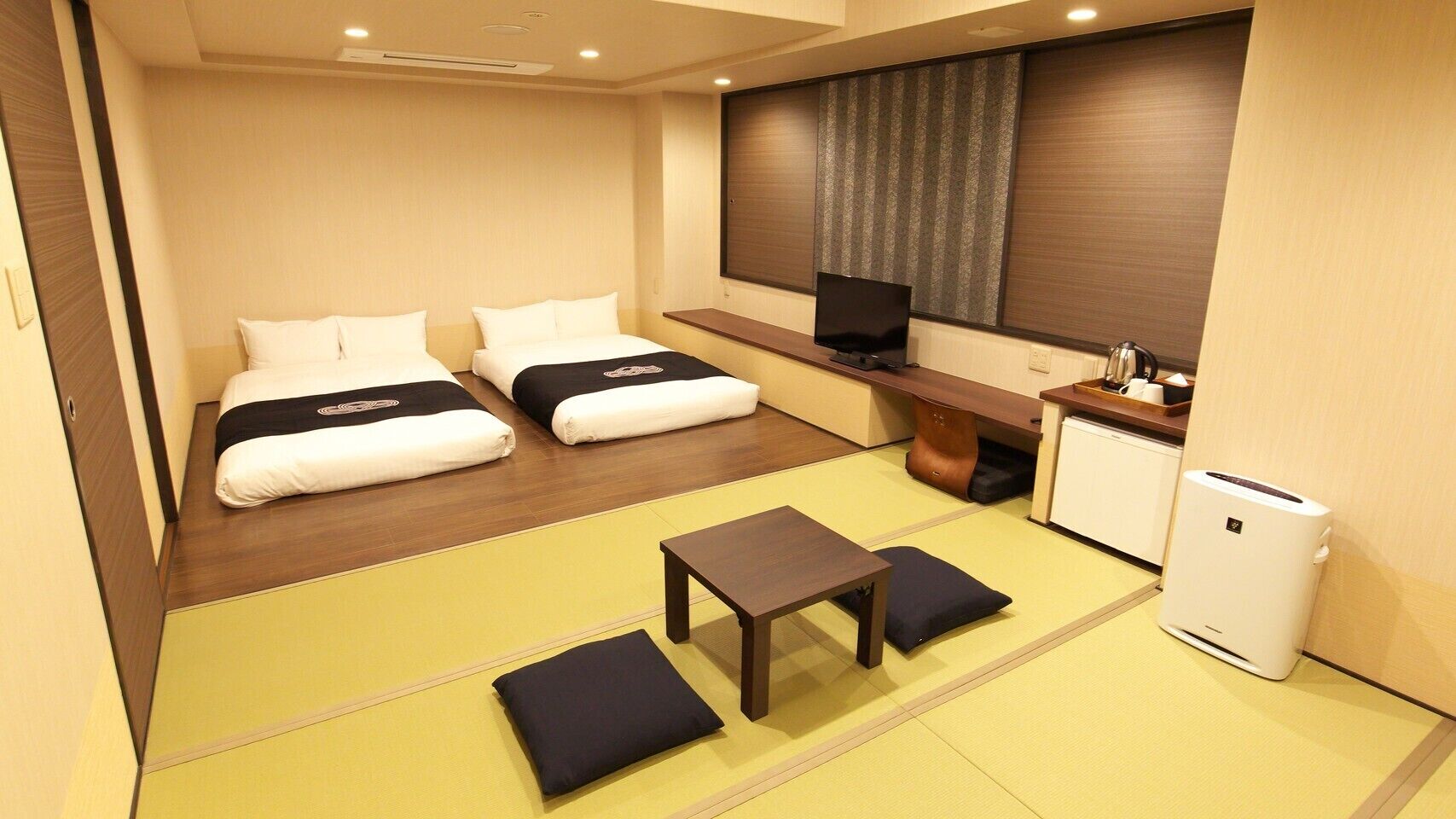 Habitación de hotel con dos camas, una mesita, un televisor y una kitchenette.